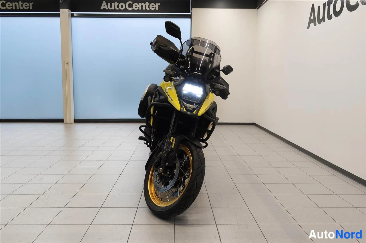 Edestä: Suzuki V-Strom 1050 edestäpäin, LED-ajovalo päällä, tuulilasi ja kultainen etuvanne, sisätiloissa AutoCenter-tilassa.