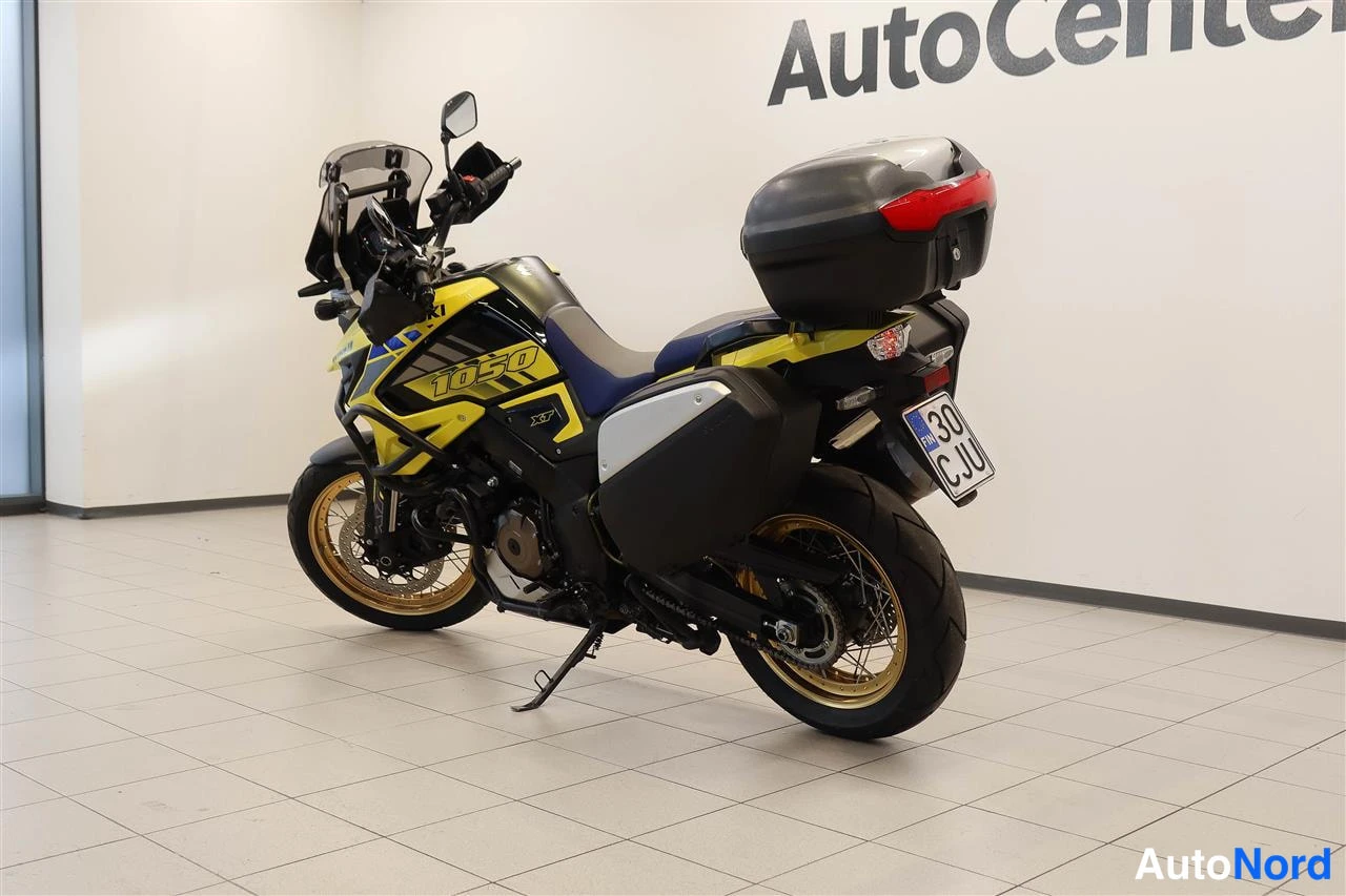 Takaviisto: Suzuki V-Strom 1050 -moottoripyörä sisätilassa takakanalta, musta laukku takana ja rekisterikilpi näkyvissä.
