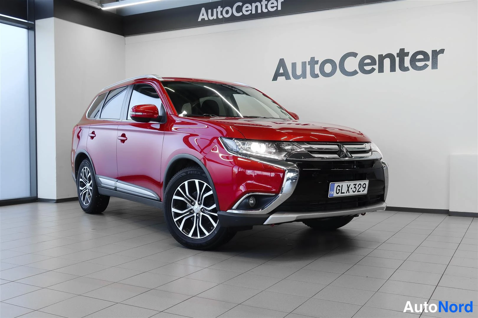 Etuviisto, nokka oikealle: Punainen Mitsubishi Outlander-etunurkkakuva sisätiloissa, rekisteritunnus näkyvissä etupuskurissa.