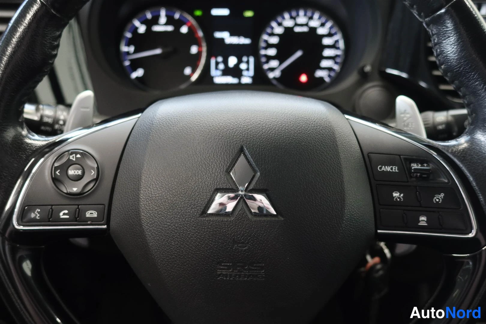 Muu: Lähikuva ohjauspyörästä: Mitsubishi-logo keskellä, painikkeita molemmin puolin ja SRS AIRBAGE-teksti, taustalla mittaristo.