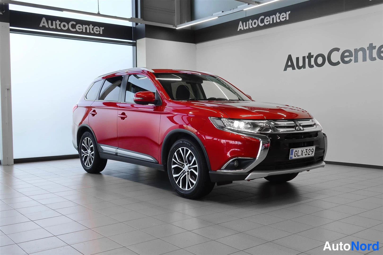 Etuviisto, nokka oikealle: Punainen Mitsubishi Outlander etunurkkakuva showroomissa, rekisteritunnus etupuskurissa.