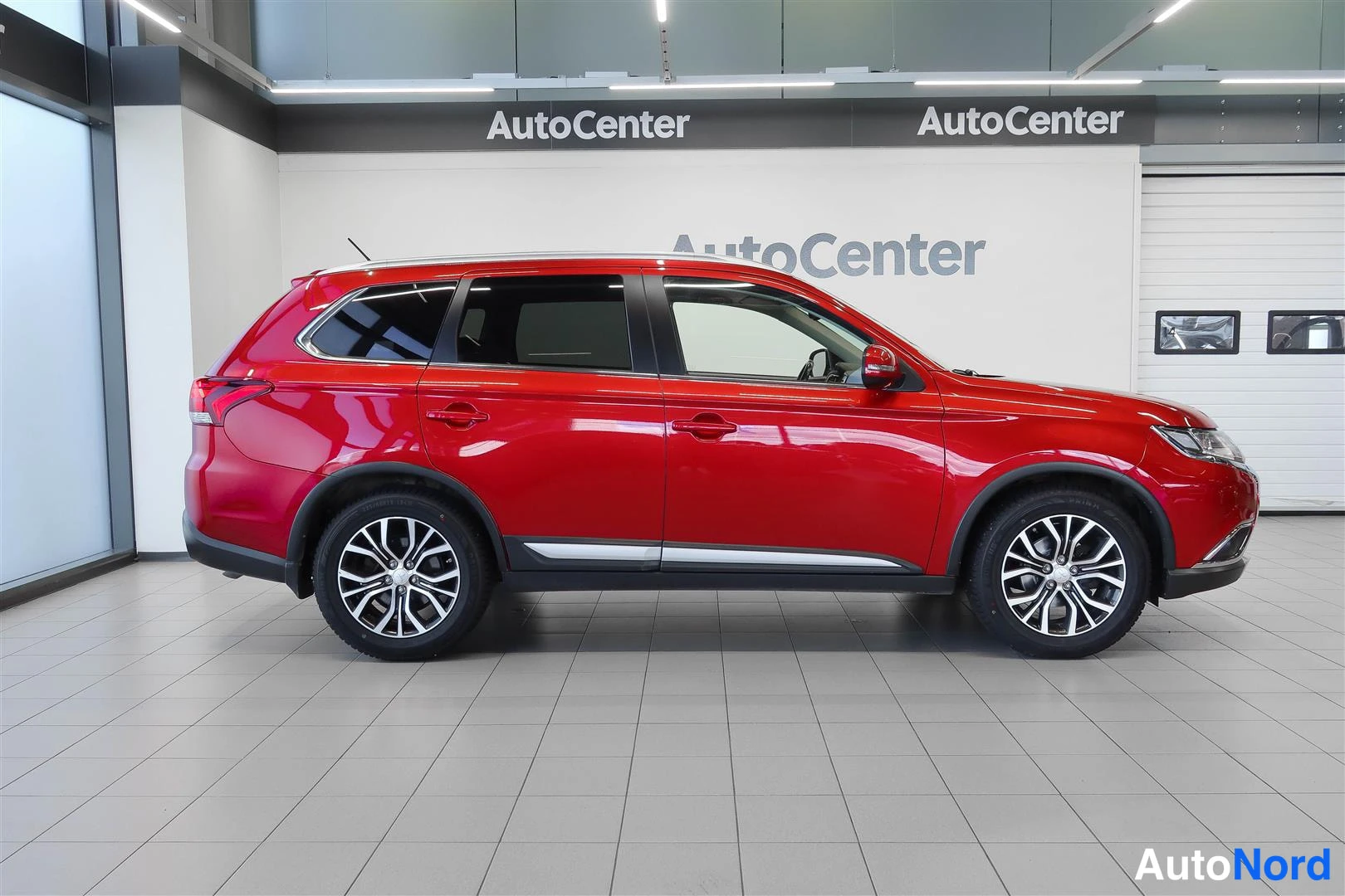 Etuviisto, nokka oikealle: Sivunurkkakuva punaisesta Mitsubishi Outlanderista showroomissa, kylki ja etuosa kuvassa.