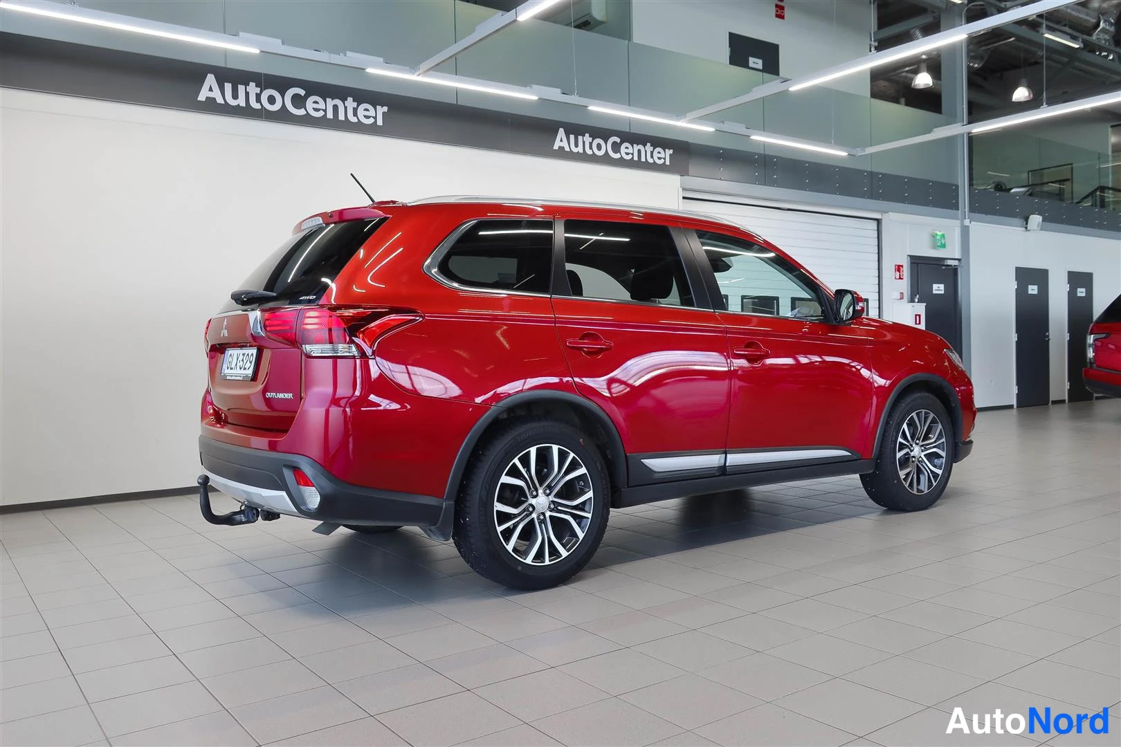 Takaviisto: Punainen Mitsubishi Outlander takaa ja oikeaa kylkeä kuvattuna autoliikkeen sisätiloissa; rekisterikilpi ja takakahvautettu vetokoukku näkyvät.