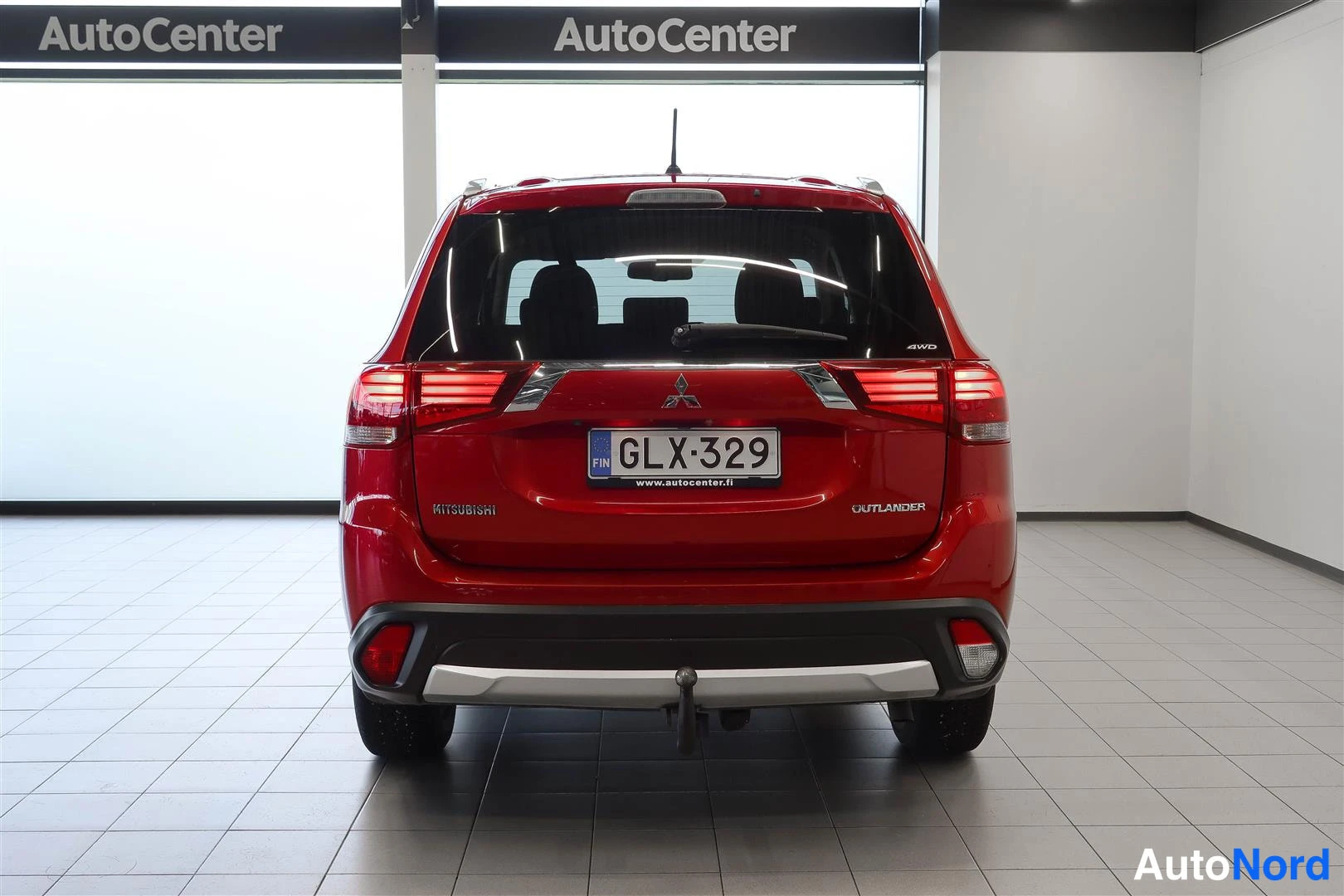 Takaa: Punaisen Mitsubishin takaosa: rekisterikilpi, takavalot ja takapuskuri näkyvissä hallitilassa.