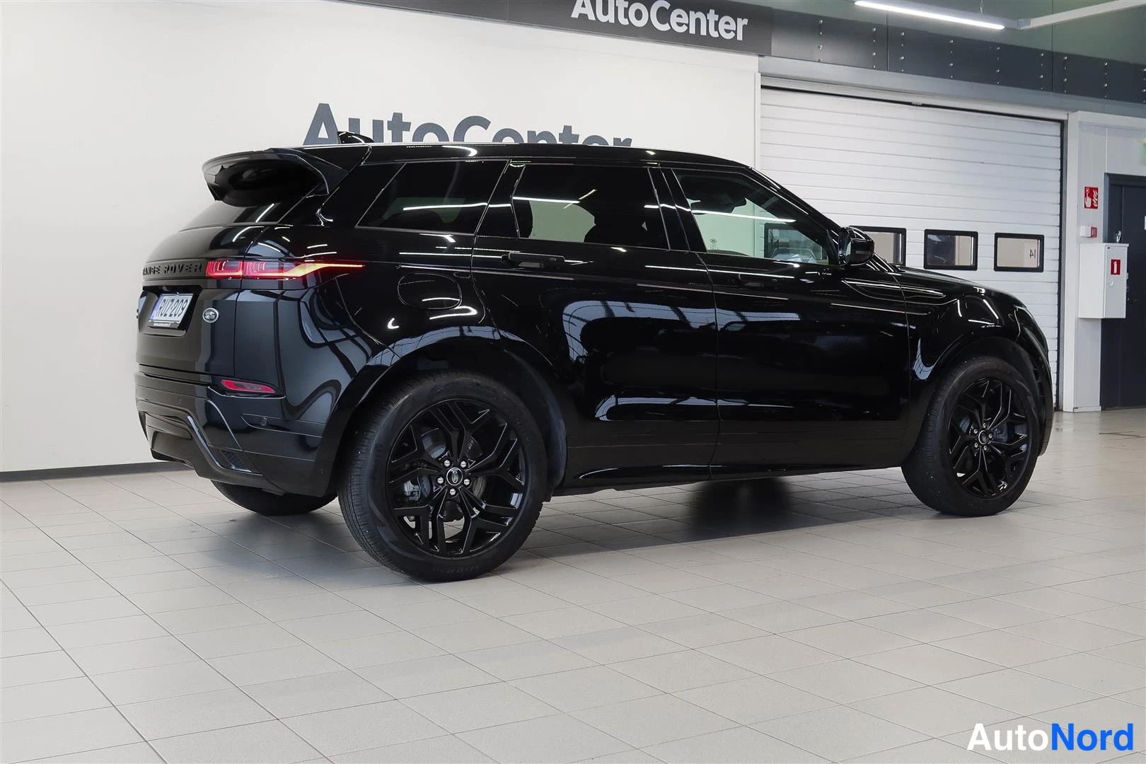 Takaviisto: Land Rover Range Rover Evoque 2023, musta, takakulma oikealta; takavalo ja mustat vanteet näkyvissä näyttämöhallissa.