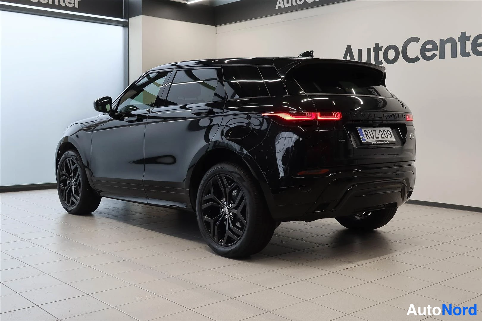 Takaviisto: Land Rover Range Rover Evoque 2023, musta, takakulma vasemmalta; takavalot ja rekisteritunnus näkyvät näyttämöhallissa.