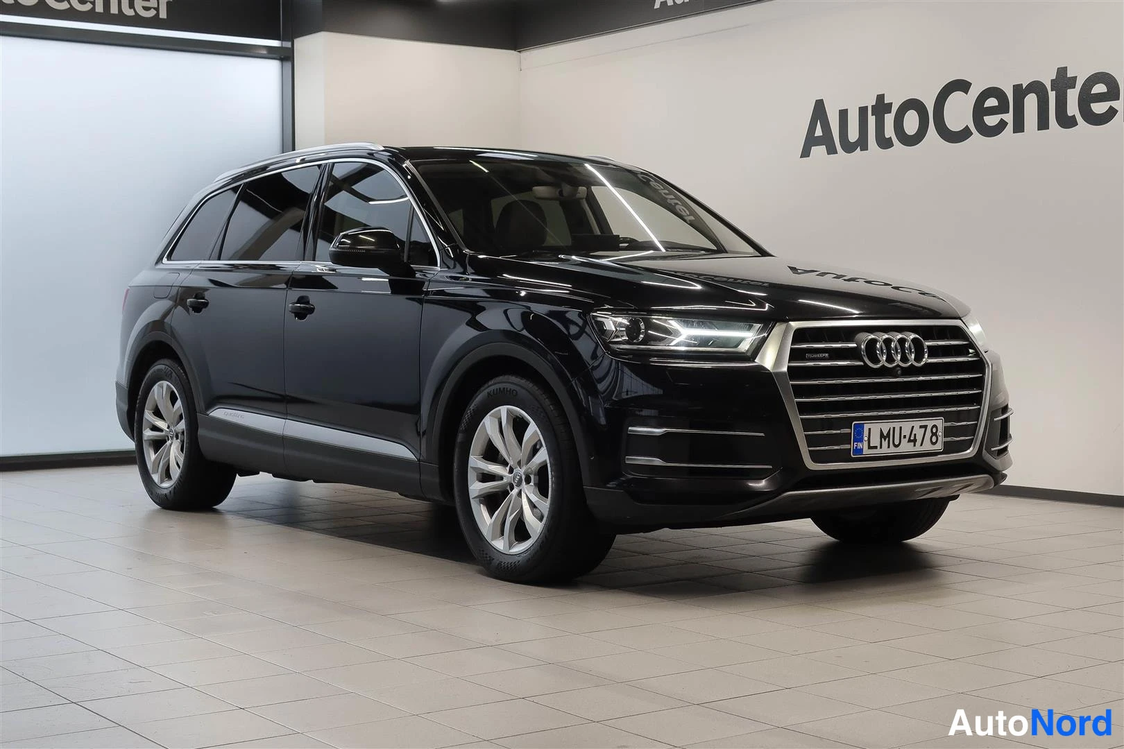 Etuviisto, nokka oikealle: Musta Audi Q7 etuviistosta vasemmalle kääntyneenä sisätiloissa, rekisterikilpi.