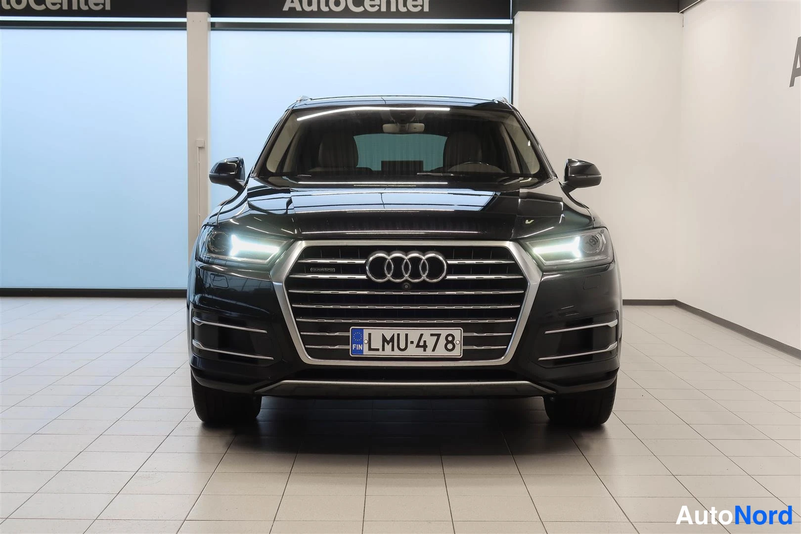 Edestä: Audi Q7:n musta keulakuva suoraan edestä, ajovalot päällä, rekisterikilpi.