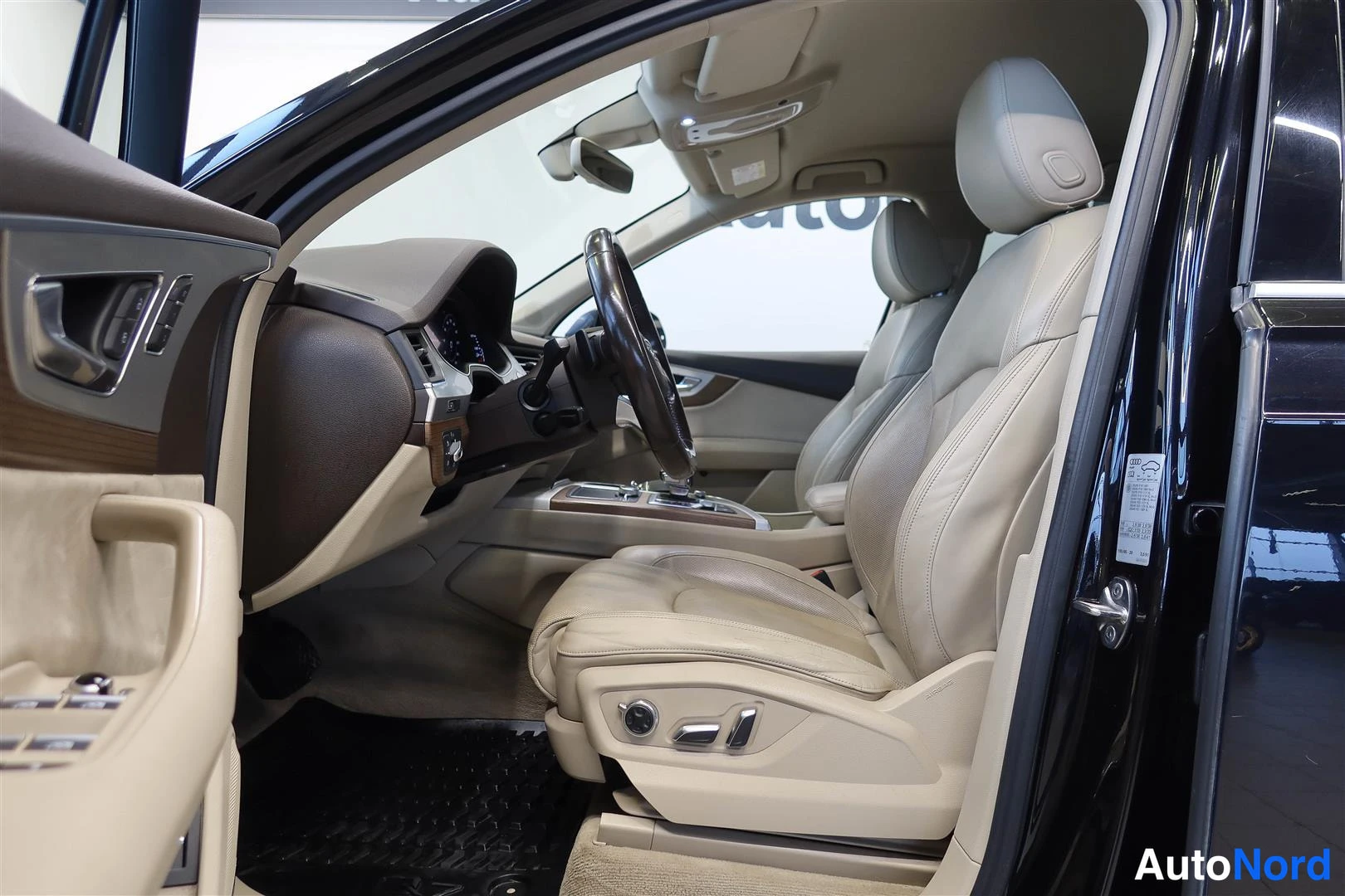 Muu: Audi Q7:n etuistuimien ja kojelaudan sisänäkymä ovilta auki; vaalea nahkap verhoilu, kaksivärinen ohjauspyörä ja matkustajanistuin.