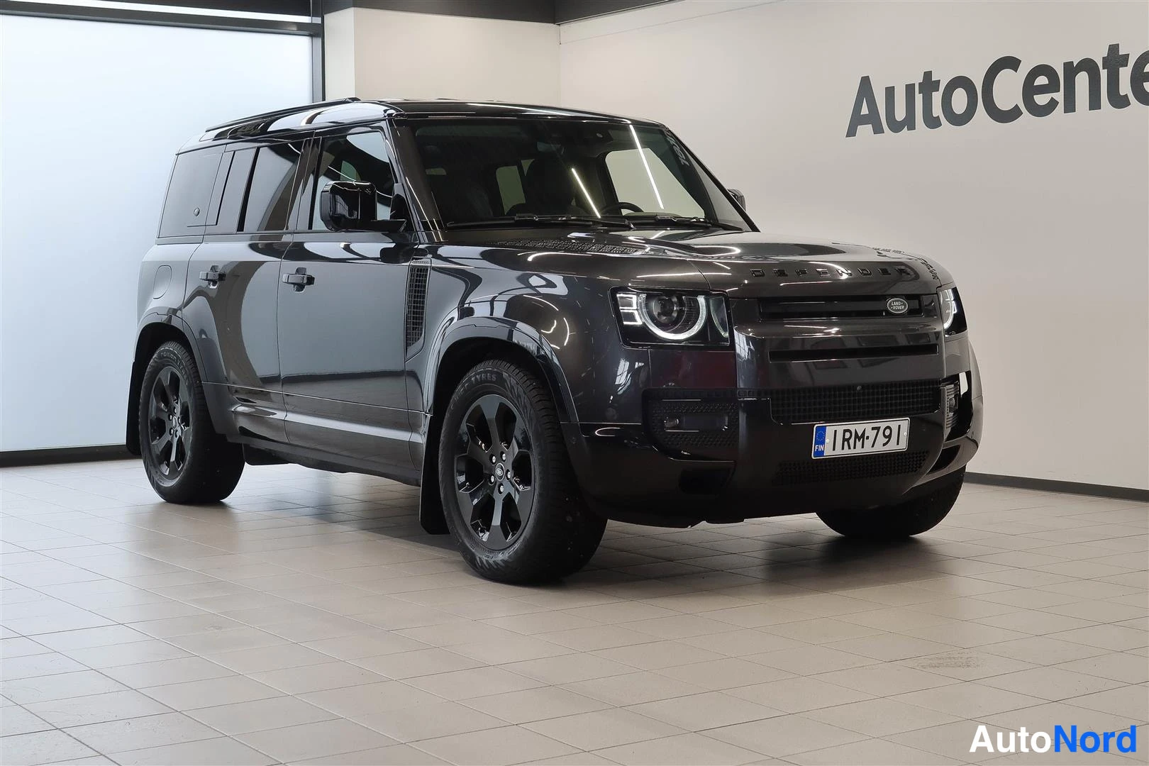 Etuviisto, nokka oikealle: Land Rover Defender 110 -maast-auto hieman vasemmalta etukulmasta kuvattuna, tummanharmaa kori, mustat kiiltävät vanteet, rekisteritunnus RM-791.