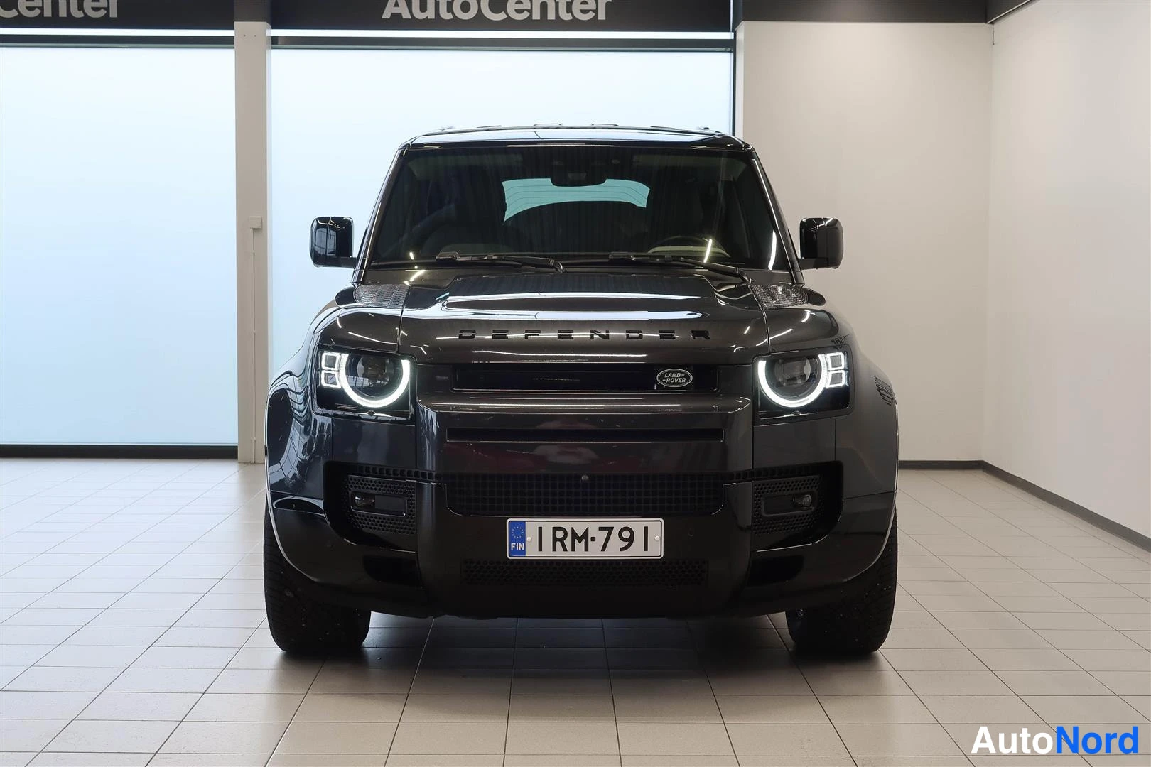 Edestä: Land Rover Defender 110 -maast-auto suoraan edestäpäin kuvattuna, tummanharmaa kori, REKISTERITUNNUS RM-791, LED-ajovalot päällä.