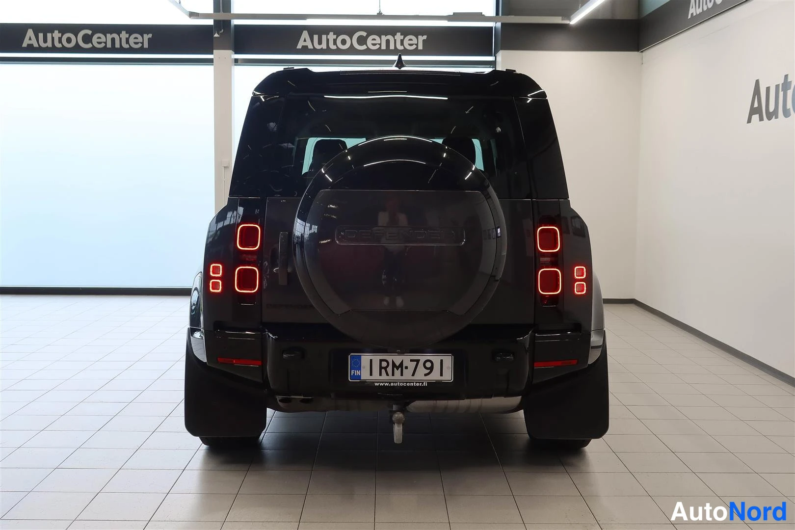 Takaa: Land Rover Defenderin takaosa autonhallissa, varapyörä kannessa ja rekisteri.