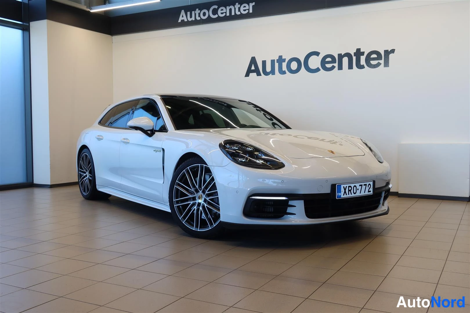 Etuviisto, nokka oikealle: Porsche Panamera Sport Turismo etuviistossa oikealta, valkoinen henkilöauto AutoCenter-hallissa, rekisterikilpi