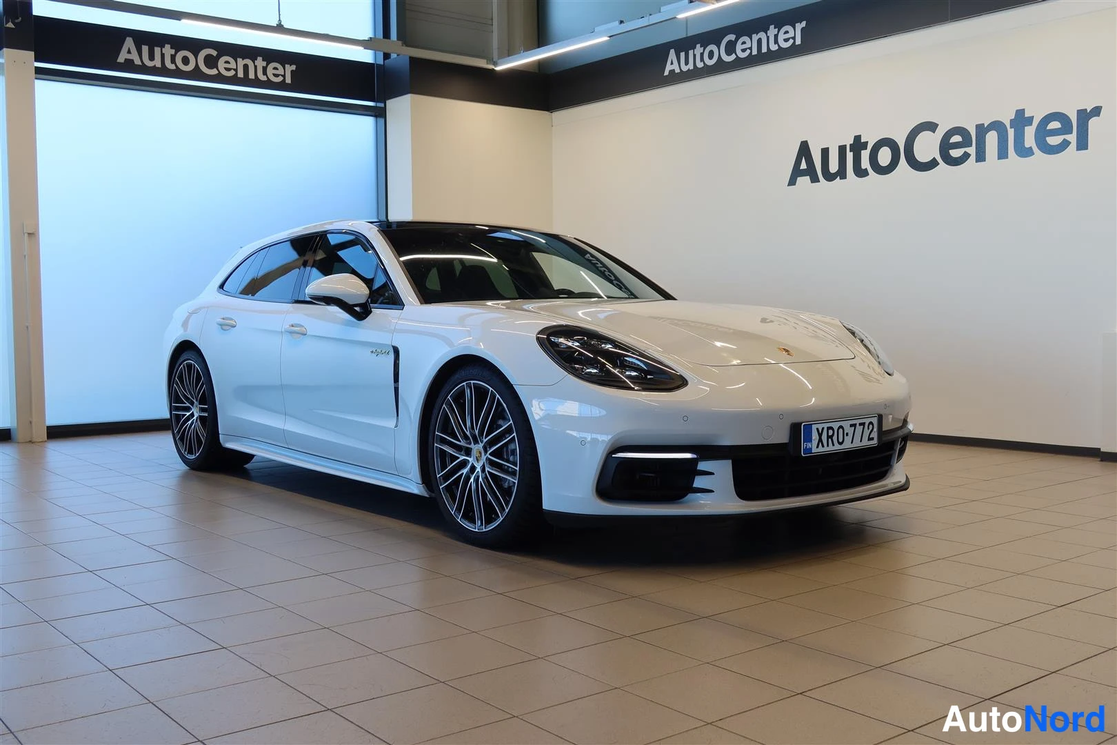 Etuviisto, nokka oikealle: Porsche Panamera Sport Turismo etuviistossa oikealta, valkoinen henkilöauto AutoCenter-hallissa