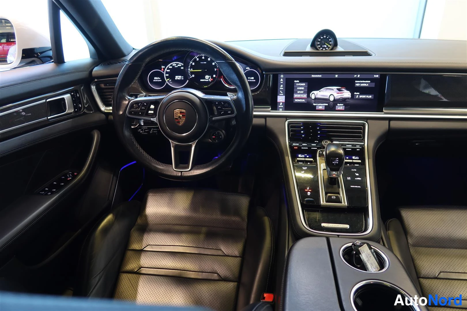 Muu: Ohjaamo keskeltä: Porsche-ohjauspyörä, mittaristo, keskinäyttö ja keskikonsoli vaihtajanappulalla