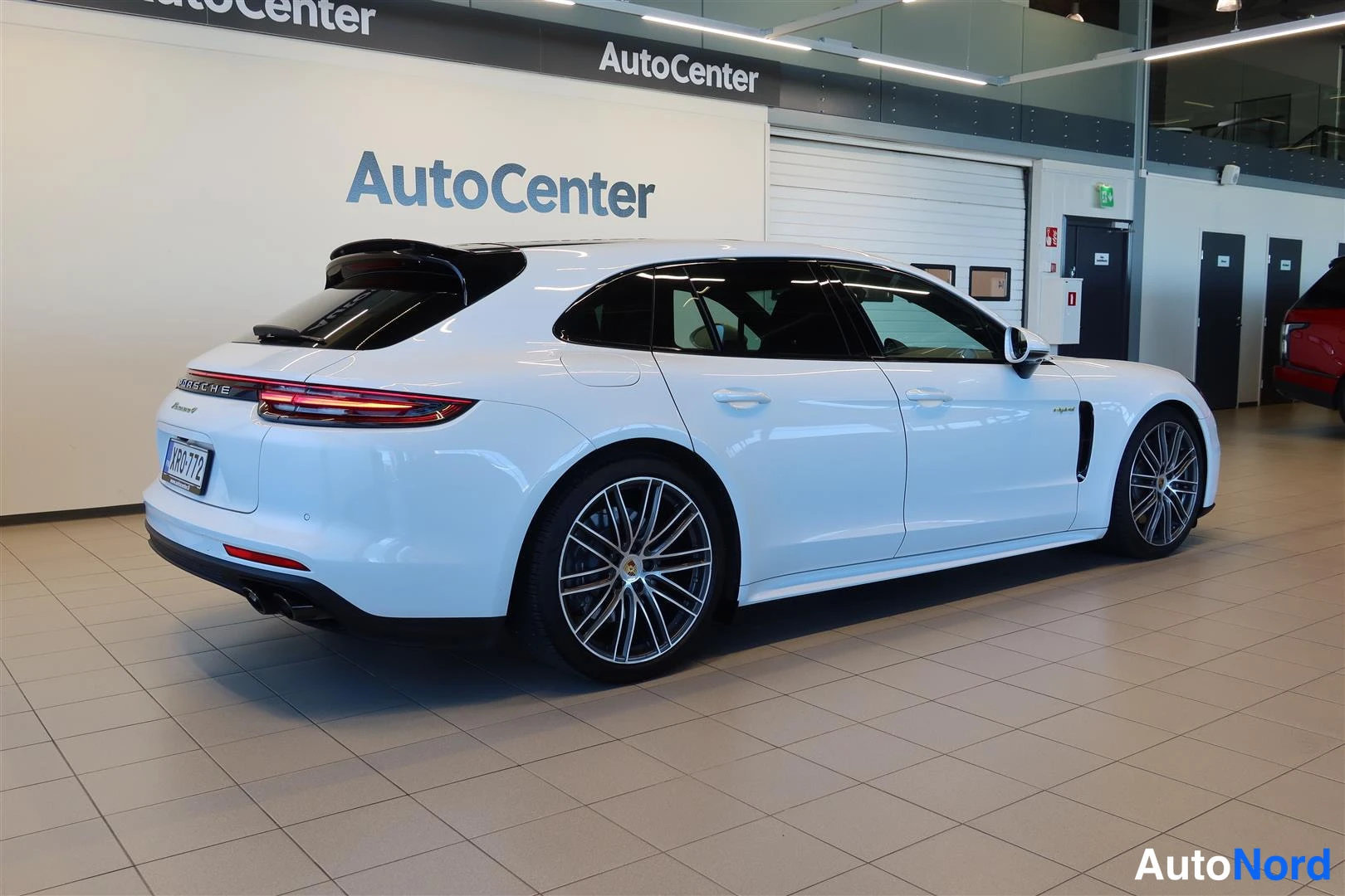 Takaviisto: Porsche Panamera Sport Turismo takaviistossa vasemmalta, valkoinen henkilöauto AutoCenter-hallissa, rekisterikilpi