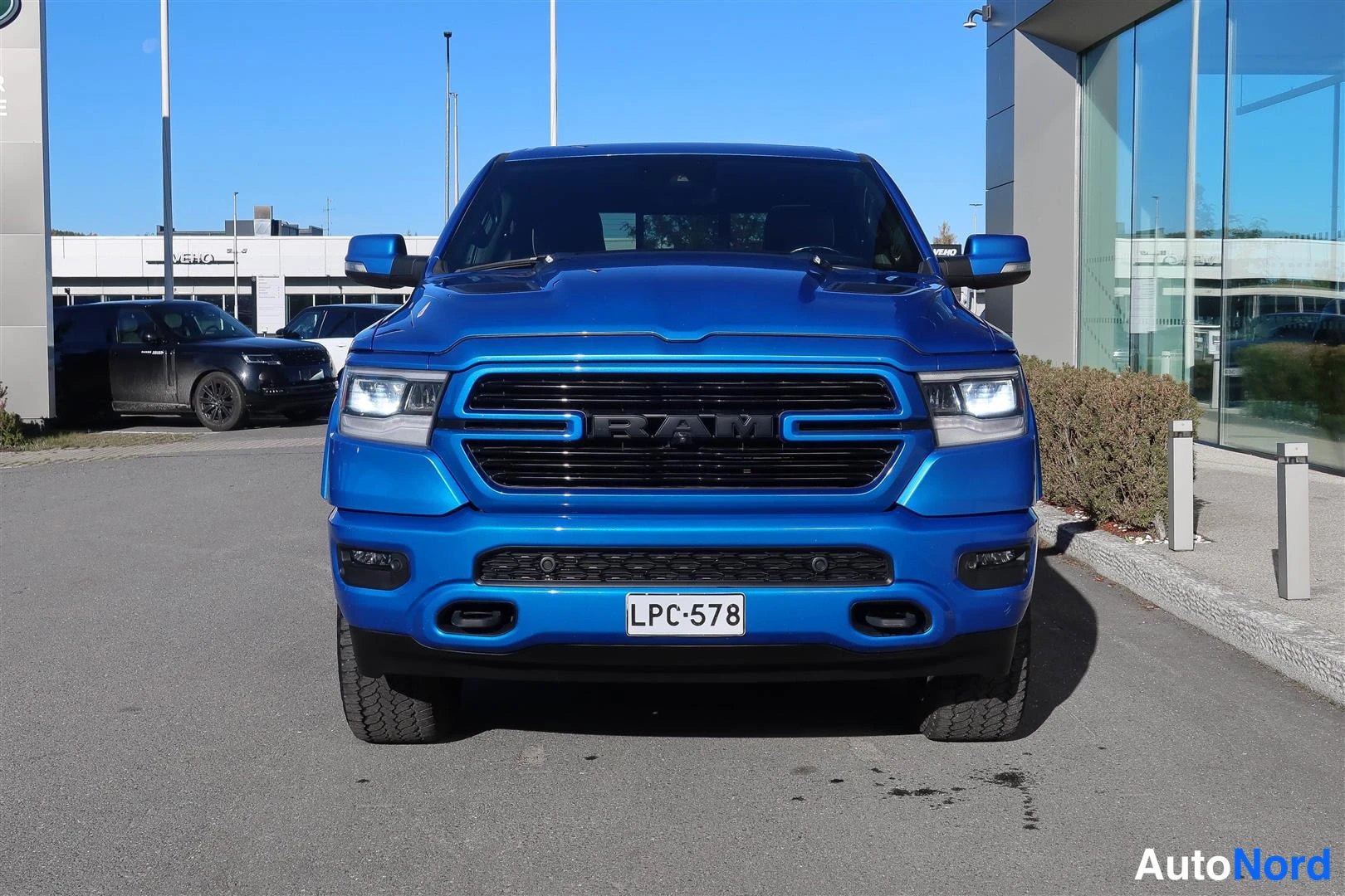 Edestä: Etupuoli-kuva sinisestä Dodge Ram -nappakuorma-autosta. Etugrilli on musta ja BAM-merkki näkyy sen keskellä. Rekisteritunnus.