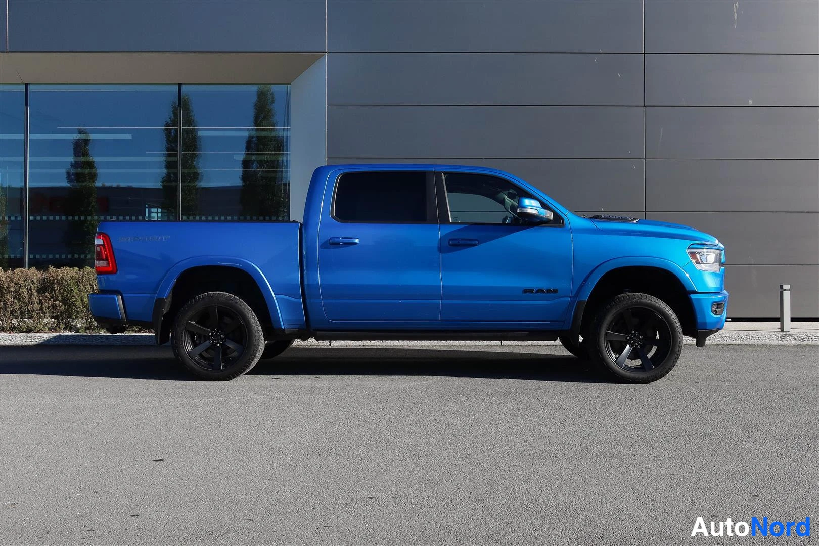 Sivulta: Sivukulma sinisestä Dodge Ram -nappakuorma-autosta. Auton oikea kylki näkyy, mustanvliset vanteet.
