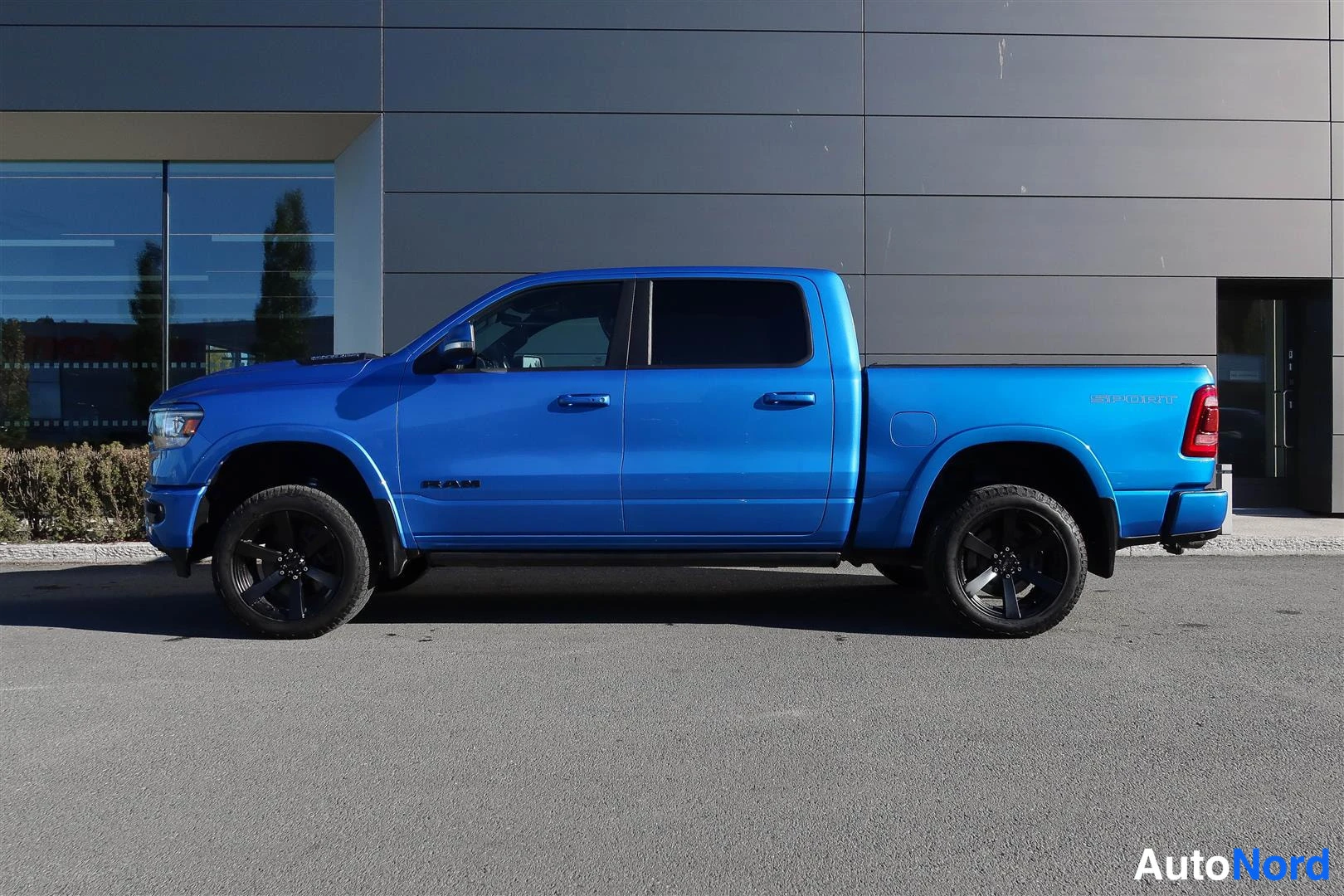 Sivulta: Sivukulma sinisestä Dodge Ram -nappakuorma-autosta. Auton vasen kylki näkyy, mustanvliset vanteet.
