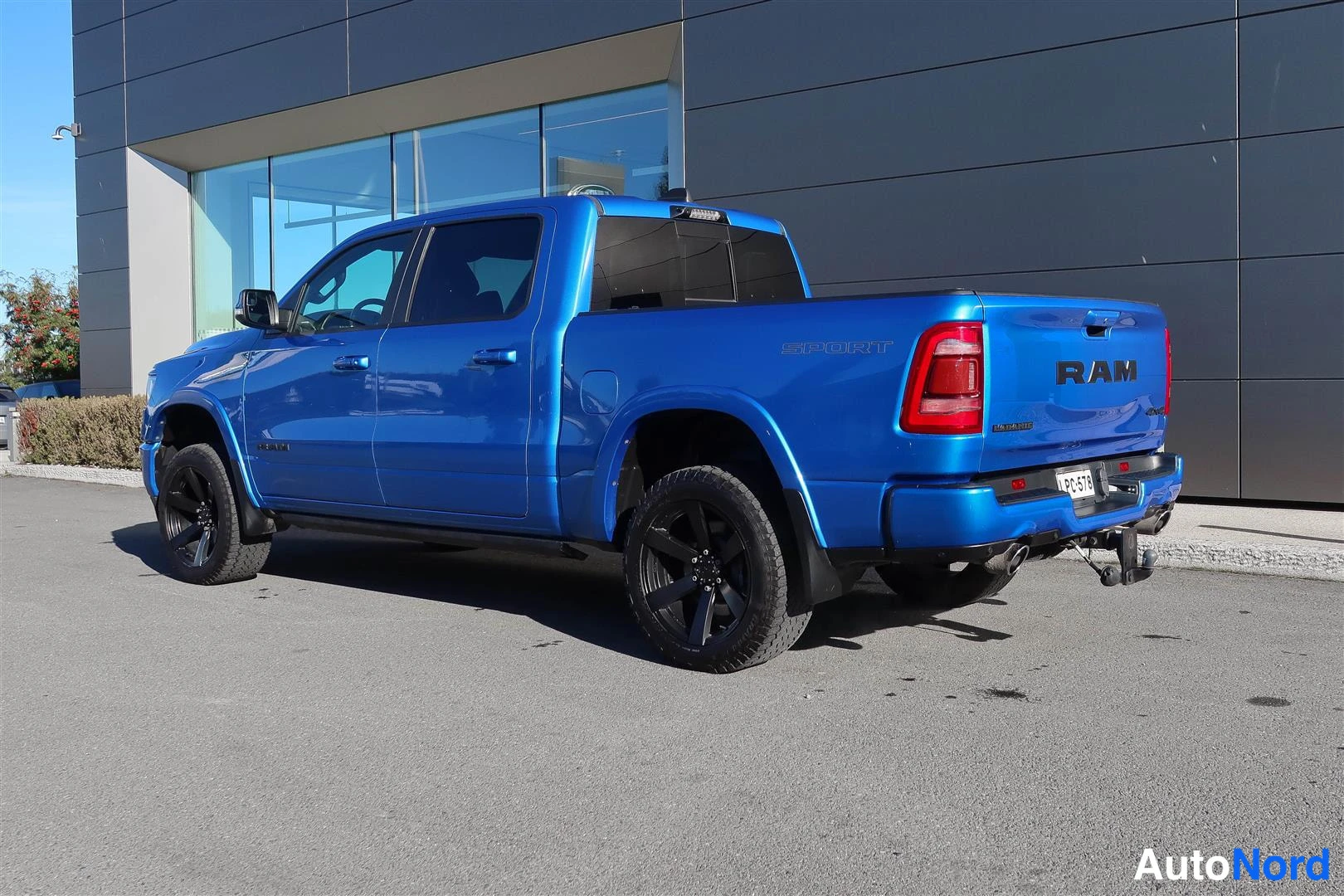 Takaviisto: Sininen pick-up-auto takaviistosta kuvattuna; peräosassa RAM-teksti, spoilerissa SPORT-teksti, mustat vanteet ja hinattava ajoneuvon takaosassa. Rekisteritunnus