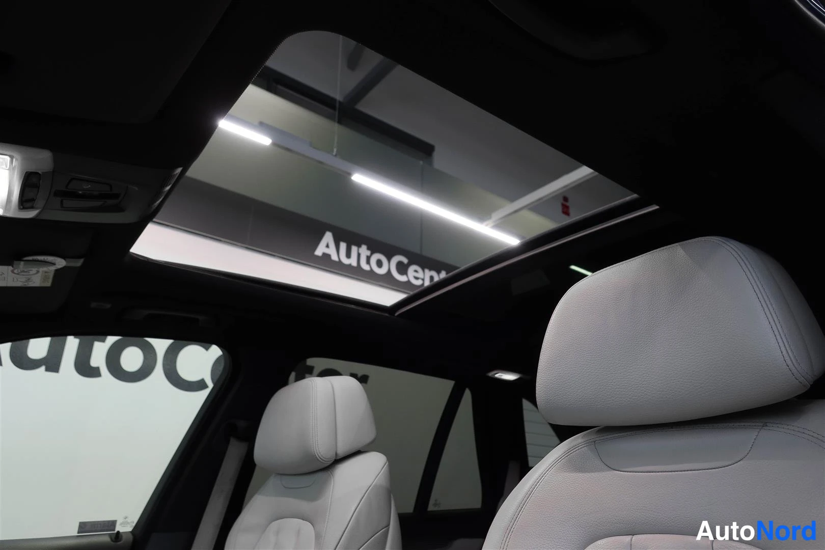 Muu: Auton sisätilat: avattu panoraamakatto ja vaaleanbeigit istuimet, taustalla showroomin AutoCenter-kyltti.