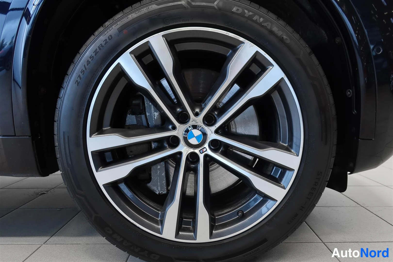 Yksityiskohta: Sivua vasten kuvattu BMW-merkkinen kevytmetallivanne paksulla renkaalla, jonka sivussa lukee 275/45ZR20.