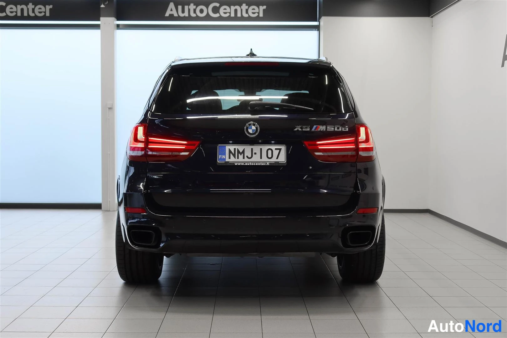 Takaa: BMW X5:n takaosa näkyy suoraan takaa showroomissa; rekisterikilpi ja X5 M50d-merkintä takaluukussa.