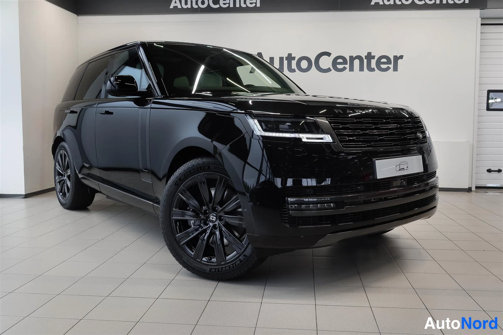 Etuviisto, nokka oikealle: Musta Range Rover -maasturi etuviistöstä Autocenter-tilassa, kiiltävä musta maali ja mustat kevytmetallivanteet.