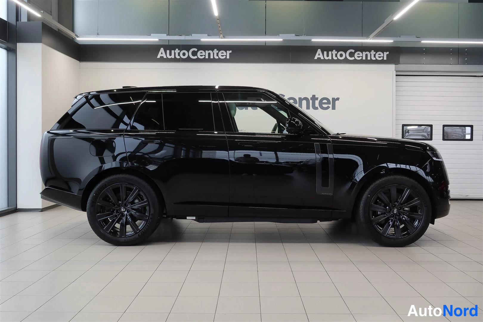 Sivulta: Musta Range Rover -maasturi sivulta kuvattuna sisätilassa, tummat ikkunat ja mustat kevytmetallivanteet.