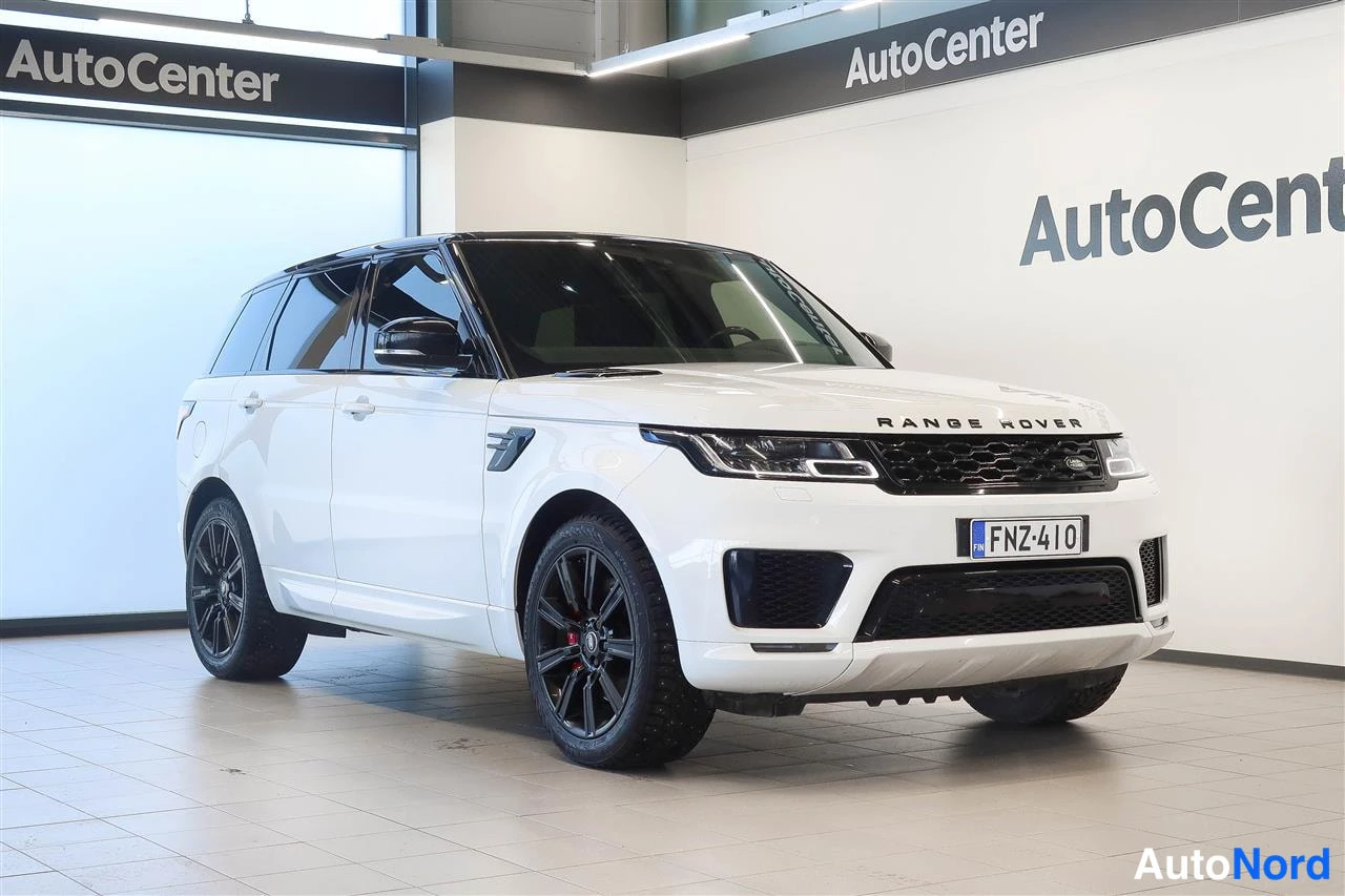Etuviisto, nokka oikealle: Valkoinen Land Rover Range Rover Sport -maastoajoneuvo etuviistosta autosalissa, rekisteritunnus, mustat vanteet ja musta katto.