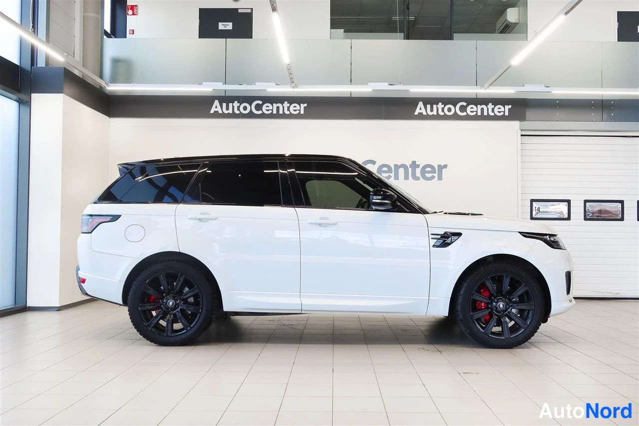 Sivulta: Valkoisen Land Rover Range Rover Sport -maastoajoneuvon sivunäkymä autosalissa, musta katto ja mustat vanteet, punaiset jarrusatulat näkyvissä.