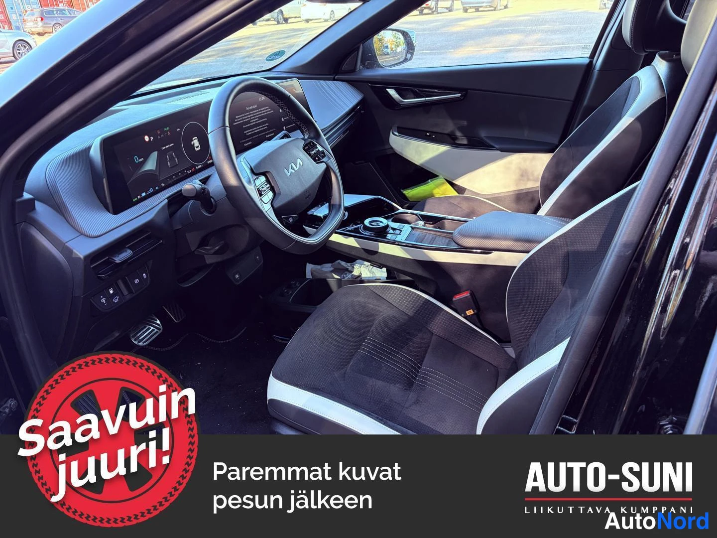Muu: Mustan Kia EV6:n etuohjaamo ja matkustajanpenkki sisältä. Kuva sisältää mainostekstin 'Saavuin juuri!' ja teksti 'Paremmat kuvat pesun jälkeen'.