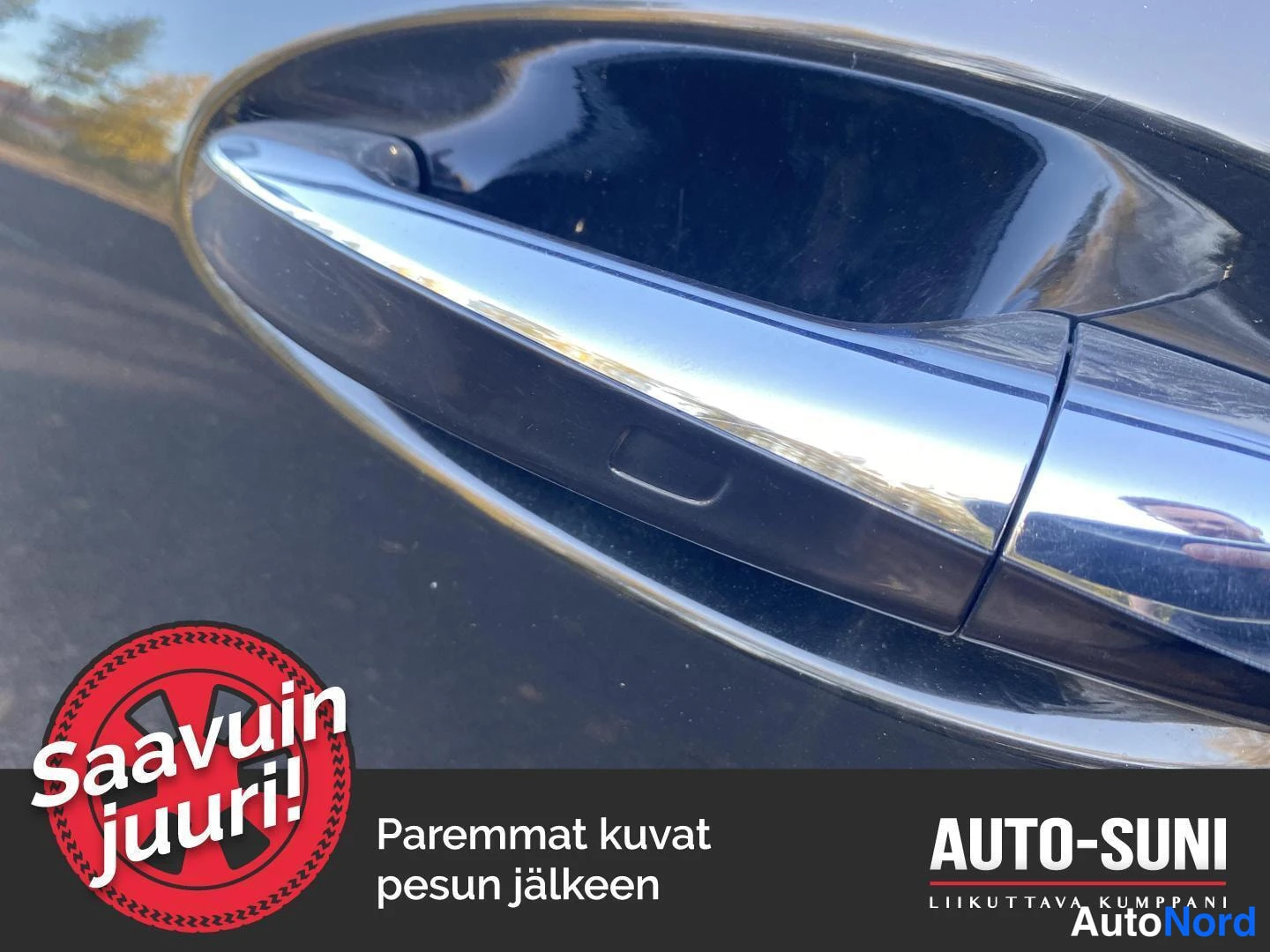 Yksityiskohta: Auton oven kahvan lähikuva, kiiltävä kromipinta, tausta tummaa pintaa.