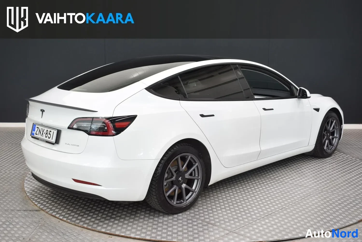 Takaviisto: Tesla Model 3 -sedanin takakulma valkoisena, rekisterikilpi ja Dual Motor -merkintä takaluukussa
