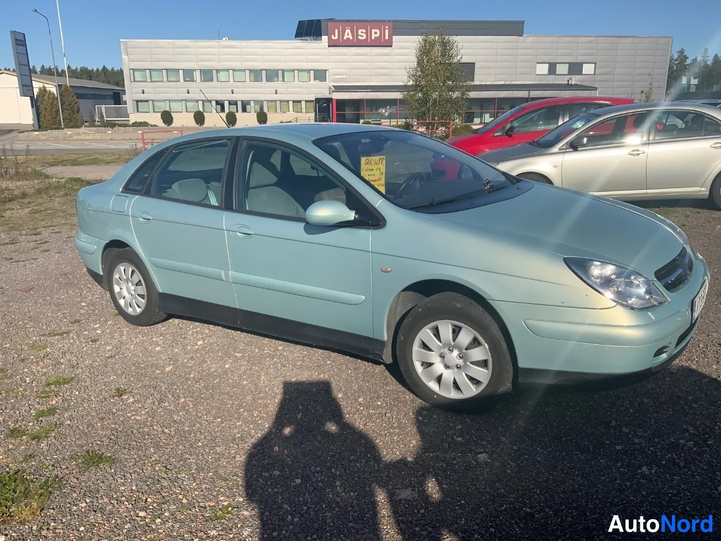 Etuviisto, nokka oikealle: Citroën C5 viistoperä vaaleanvihreänä kolmannelta sivulta; kylki, etusäleikkö ja peilit näkyvät, auto parkkeerattuna soratontille muiden autojen viereen.