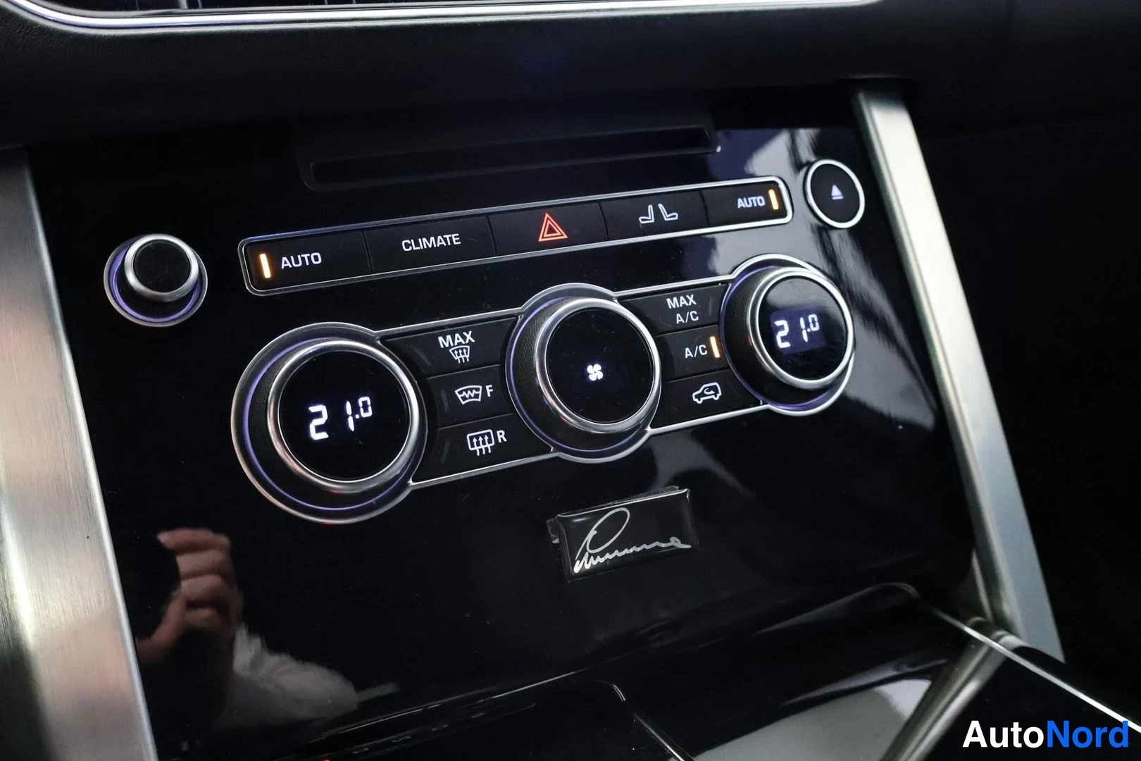Yksityiskohta: Keskikonsolin ilmastointipaneeli, näytöt näyttävät 21°, merkkivalot AUTO, CLIMATE, MAX A/C ja A/C.