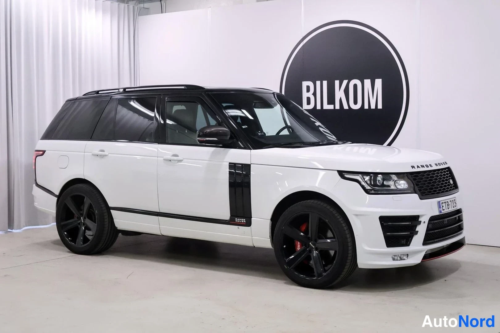 Etuviisto, nokka oikealle: Valkoinen Range Rover etuviistosta oikealta sisätiloissa, BILKOM-tunnus taustalla.