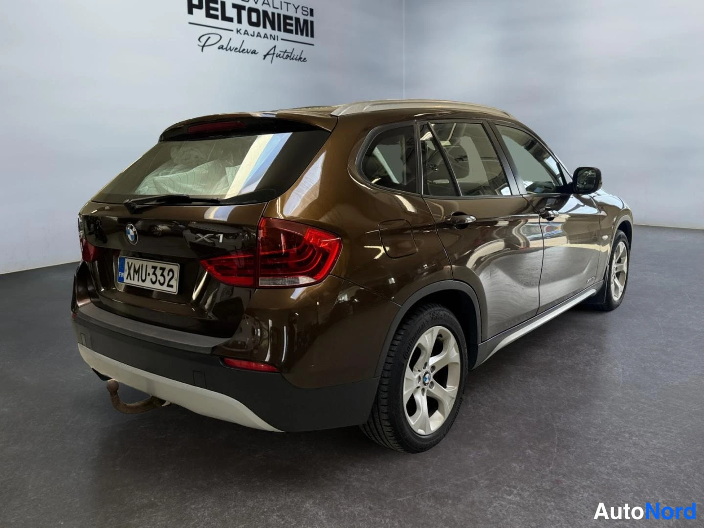 Takaviisto: BMW X1 takaapäivännosto vasemmalle, rekisteritunnus, perävaunukoukku näkyy.