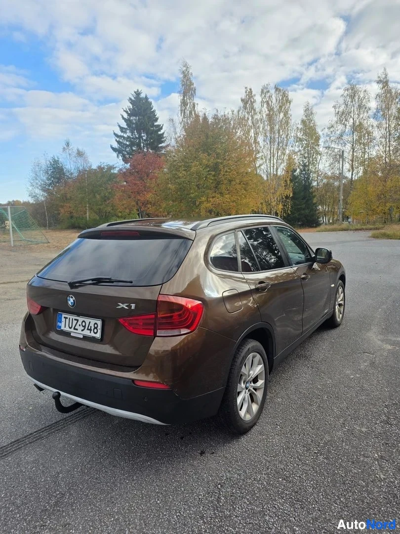 Takaviisto: Ruskean BMW X1:n takakulman kuva, takamoottoritie näkyvissä, X1-tunnus ja rekisteritunnus.