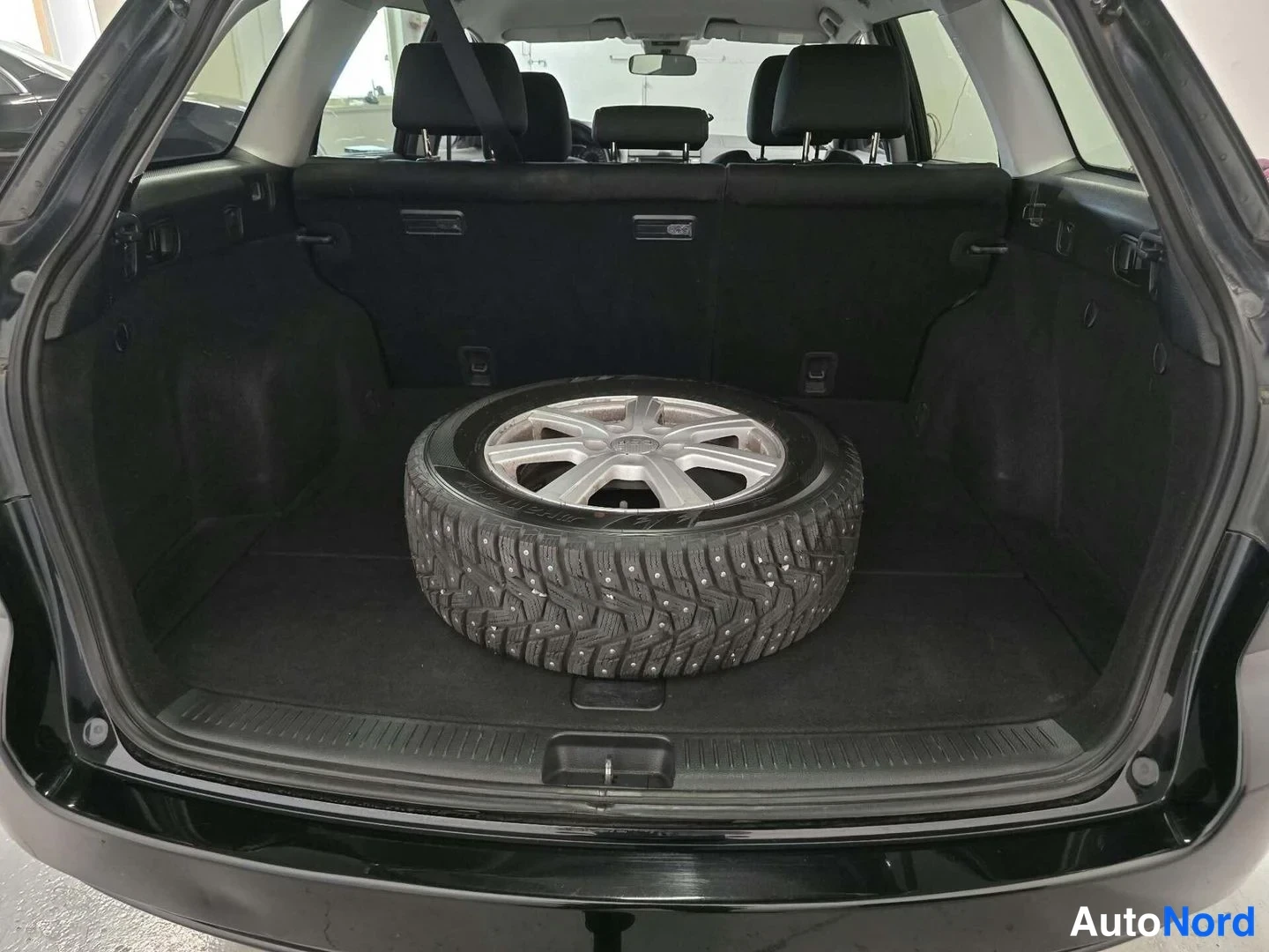 Muu: Musta Mazda 6 -farmarin avattu tavaratila, jossa on nokkarenkainen vararengas alustalla.