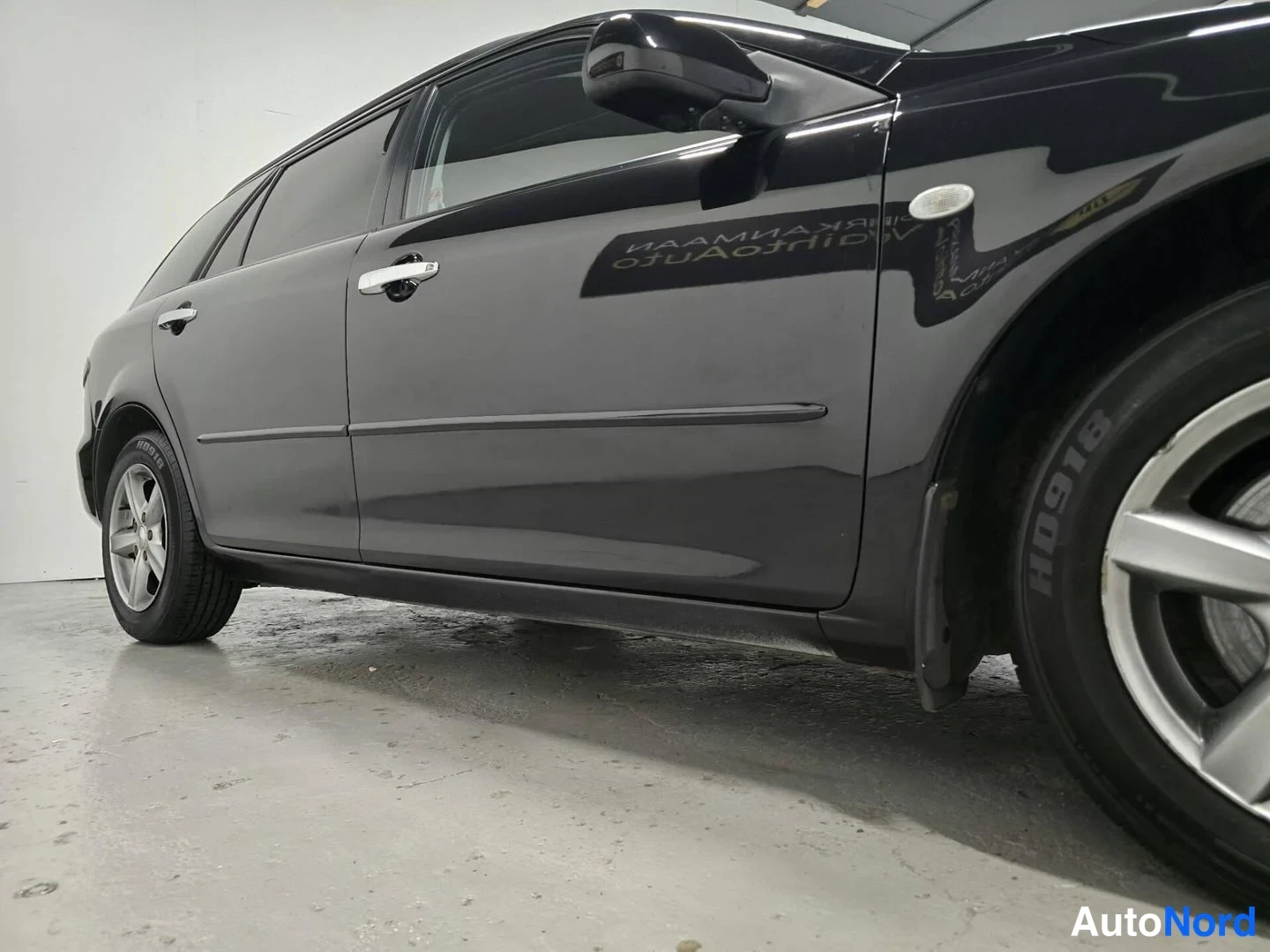 Sivulta: Mustan Mazda 6 Sport Wagonin kylki sivulta kuvattuna; pertoovi, kromiovienkahat ja takapyörä näkyvät valkoisessa tilassa.