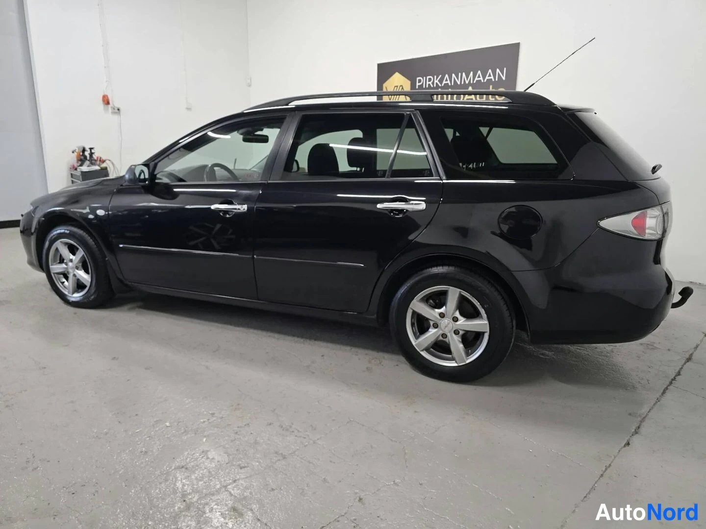 Takaviisto: Mustan Mazda 6 -farmariauton kylki ja takakulma sisätilassa, takaosasasto ja ajovalot näkyvät kuvan oikealla.