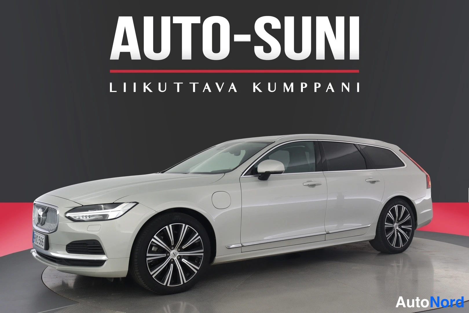 Etuviisto, nokka vasemmalle: Volvo V90 -asema-auto etukolmiconnasta vasemmalle, hopeanvärinen kori, rekisteritunnus, myyntihallin taustalla Auto-Suni-logo.