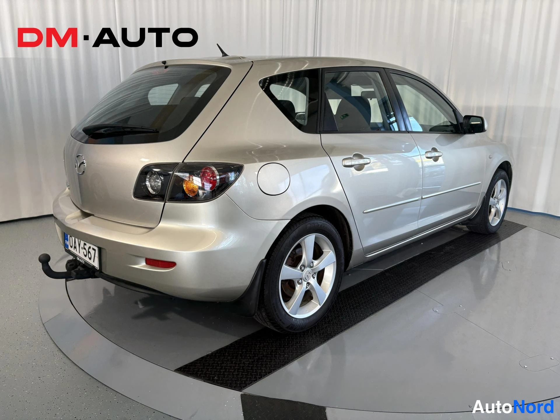 Takaviisto: Mazda 3 -farmarihatchbackin takakulmanäkymä; hopeavärinen auto, takavalojen lähikuva, rekisteritunnus, takakoukku näkyvissä.