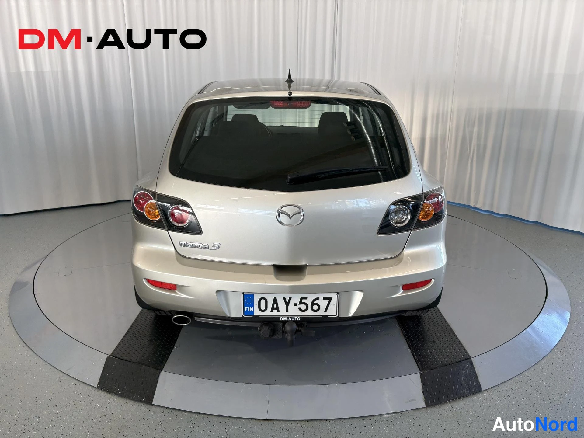 Takaa: Mazda 3:n suora takaa-ajonäkymä; hopeavärinen auto, Mazda-tunnus ja Mazda 3 -teksti takaosassa, rekisteritunnus.