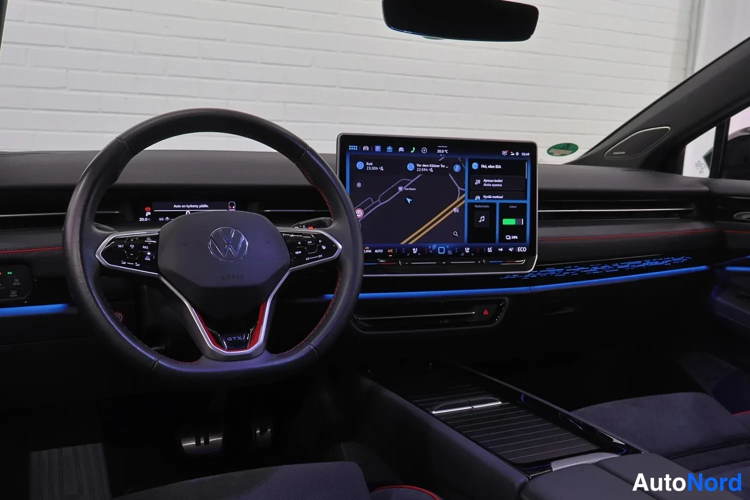 Muu: Näyttö: Volkswagenin etuohjaamo leveästä kulmasta, jossa ohjauspyörä, iso näyttö ja sininen tunnelmavalaistus.