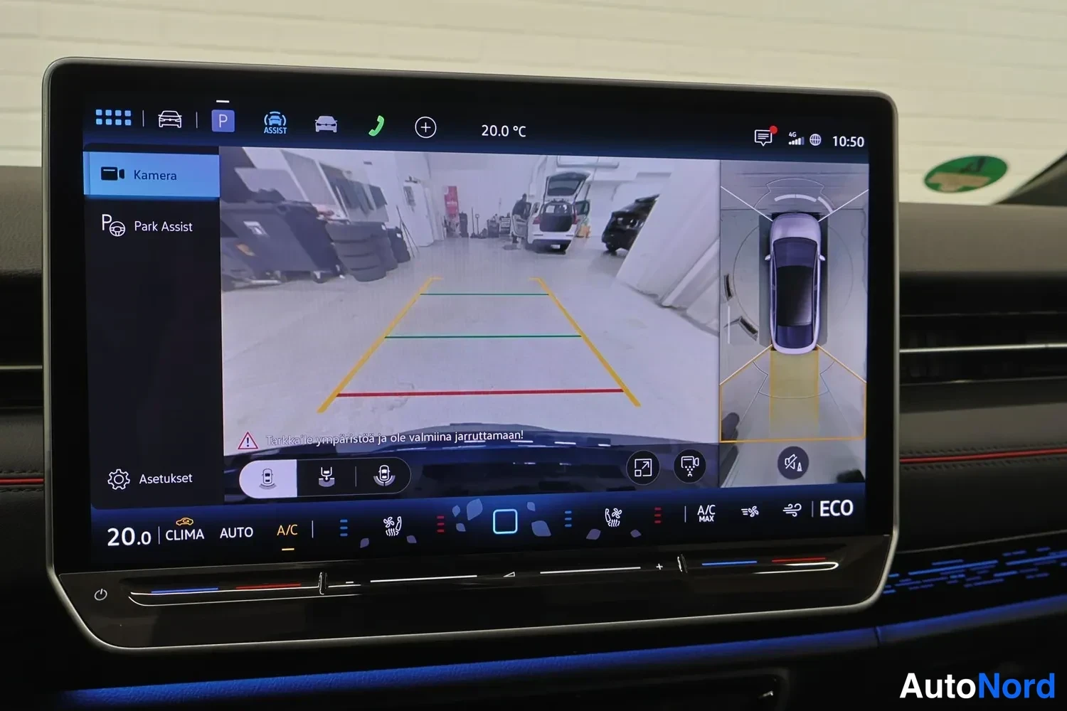 Yksityiskohta: Keskirivin infotainment-näyttö näyttää peruutuskameran kuvaa parkkitiloineen, Park Assist -valikko sekä ilmastointi- ja ECO-asetukset alareunassa.