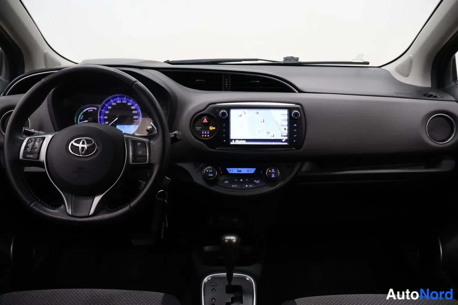 Muu: Täysi ohjaamon näkymä: Toyota-ohjauspyörä, hybridi-mittaristo, keskikonsolin kosketusnäyttö ja automaattivaihteen valitsin.