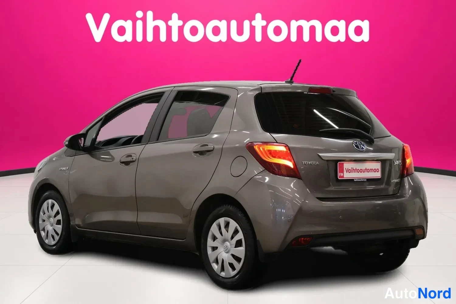 Takaviisto: Toyotan takakolmisureunus vasemmalta: harmaanruskea crossover-hatchback, punaiset takavalot ja pinkin taustan.