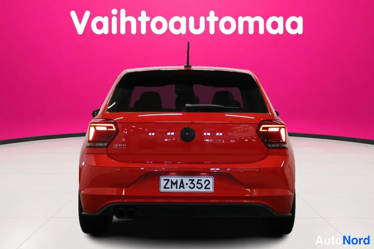 Takaa: Punaisen Volkswagenin takanäky studiossa, rekisterikilpi, sisätiloja näkyy takalasin läpi.